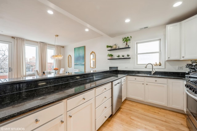 kitchen with dark stone countertops, stainless steel appliances, light wood-type flooring, sink, and decorative light fixtures