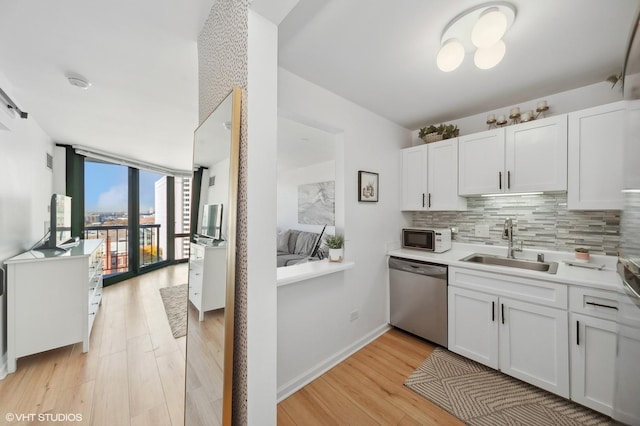 kitchen with white cabinets, sink, stainless steel dishwasher, decorative backsplash, and a wall of windows