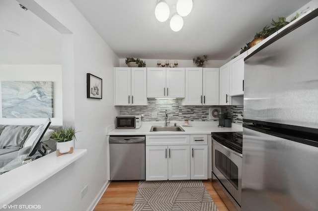 kitchen featuring sink, decorative backsplash, light hardwood / wood-style floors, white cabinetry, and stainless steel appliances