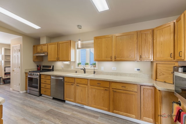 kitchen with hanging light fixtures, appliances with stainless steel finishes, sink, and light hardwood / wood-style flooring