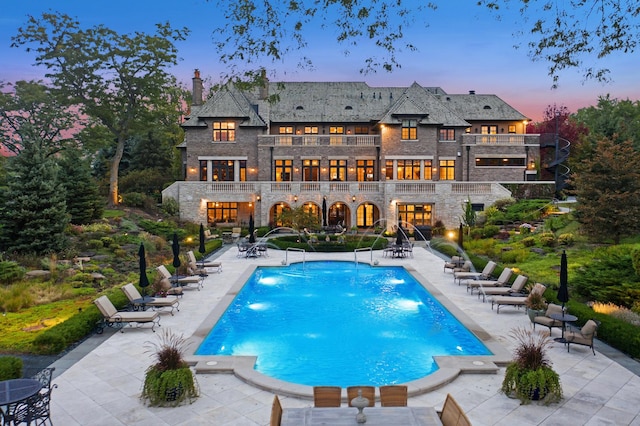 back house at dusk featuring a community pool, a patio area, pool water feature, and a balcony