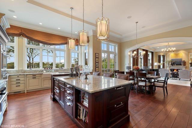 kitchen with light stone countertops, dark brown cabinetry, sink, a center island with sink, and a notable chandelier