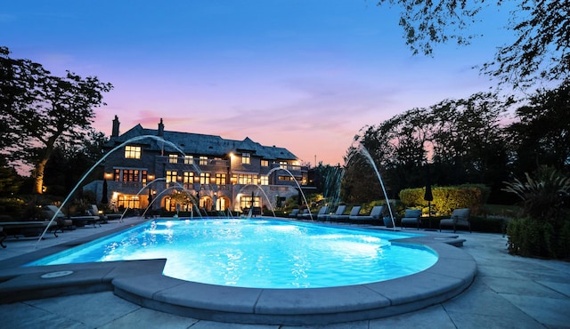 pool at dusk featuring pool water feature