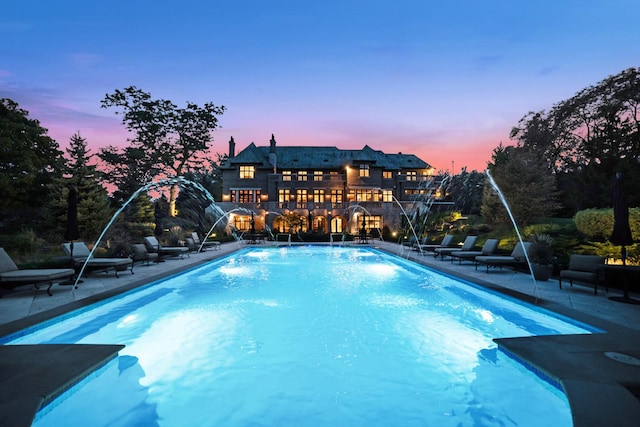 pool at dusk featuring pool water feature and a patio area