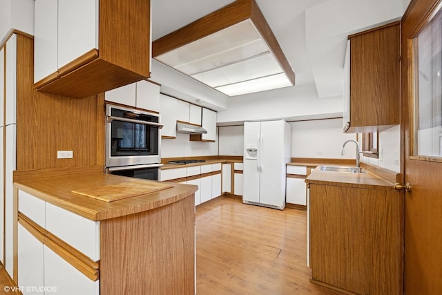 kitchen with white refrigerator with ice dispenser, light wood finished floors, a sink, gas cooktop, and under cabinet range hood