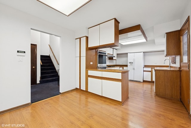 kitchen with oven, a peninsula, white refrigerator with ice dispenser, white cabinets, and light wood finished floors