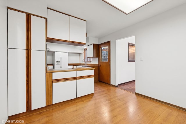 kitchen featuring white fridge with ice dispenser, light wood finished floors, white cabinetry, and baseboards