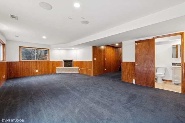 carpeted empty room featuring wooden walls, wainscoting, and visible vents