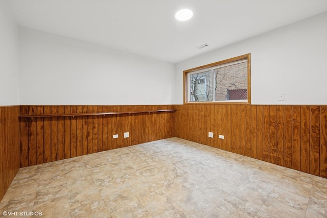 unfurnished room featuring a wainscoted wall, wood walls, and visible vents