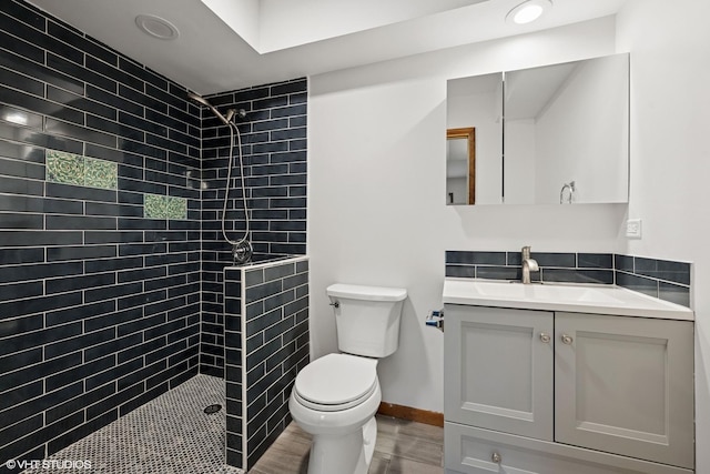 bathroom featuring toilet, wood finished floors, vanity, baseboards, and tiled shower