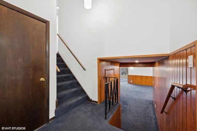 stairs with wood walls, carpet flooring, and a towering ceiling