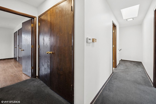 corridor featuring a skylight, carpet flooring, and baseboards