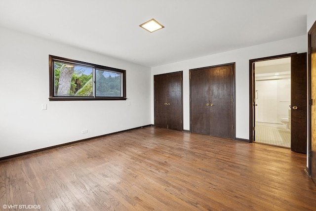 unfurnished bedroom with ensuite bath, baseboards, multiple closets, and wood finished floors