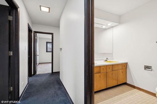 hallway with a sink, light colored carpet, and baseboards