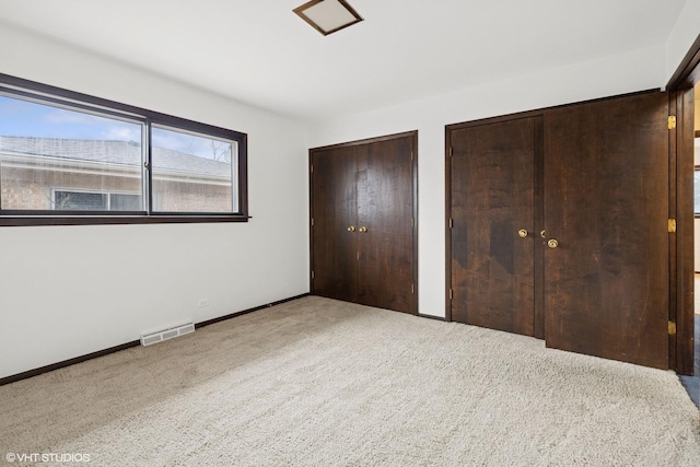 unfurnished bedroom with multiple closets, baseboards, visible vents, and carpet flooring