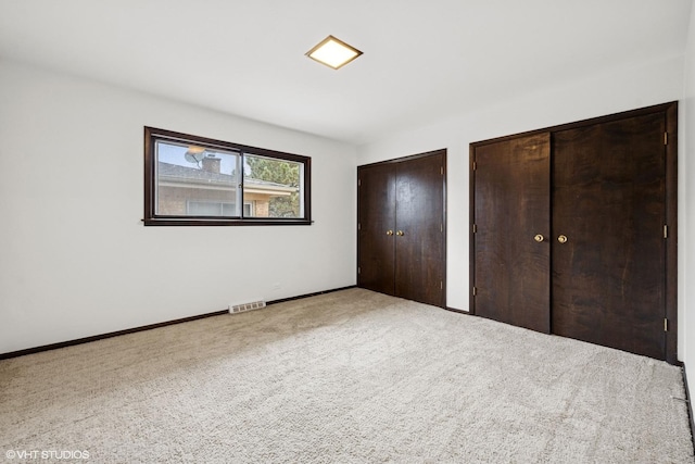 unfurnished bedroom featuring carpet flooring, two closets, visible vents, and baseboards