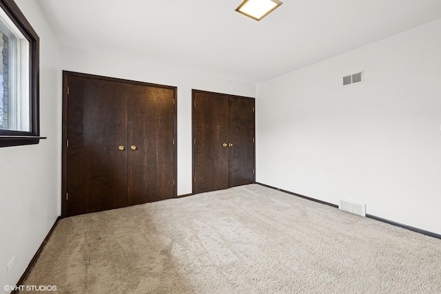 unfurnished bedroom featuring baseboards, carpet, visible vents, and multiple closets