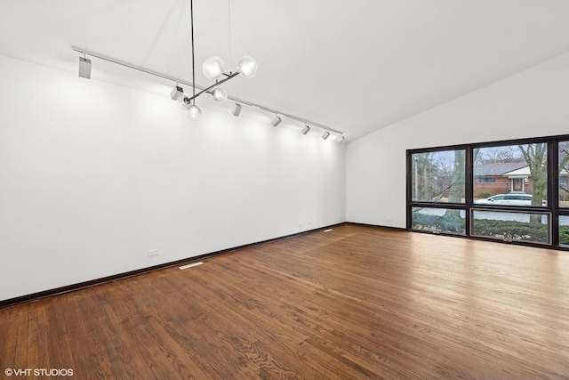 spare room featuring vaulted ceiling, baseboards, wood finished floors, and a chandelier