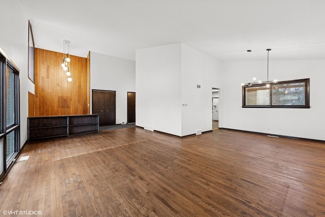 unfurnished living room with a notable chandelier, visible vents, high vaulted ceiling, and wood finished floors