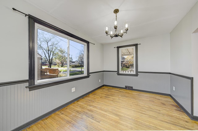 spare room with hardwood / wood-style flooring, plenty of natural light, and a chandelier