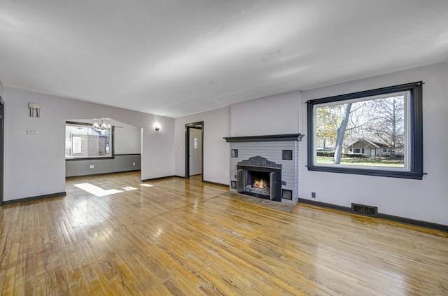 unfurnished living room with hardwood / wood-style floors, a notable chandelier, and a fireplace