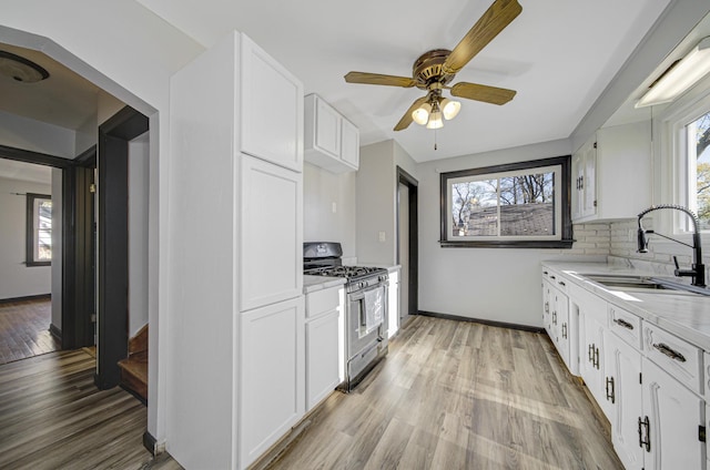 kitchen featuring light wood-type flooring, white cabinetry, stainless steel gas range oven, and sink