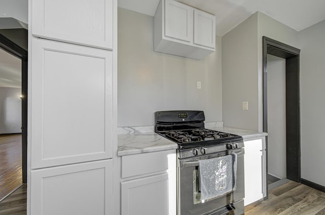 kitchen featuring white cabinets, gas stove, light stone counters, and wood-type flooring