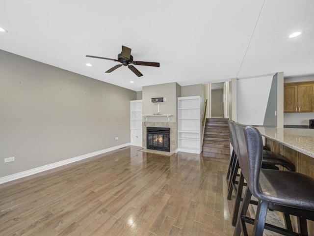 living room with a tiled fireplace, ceiling fan, and light wood-type flooring