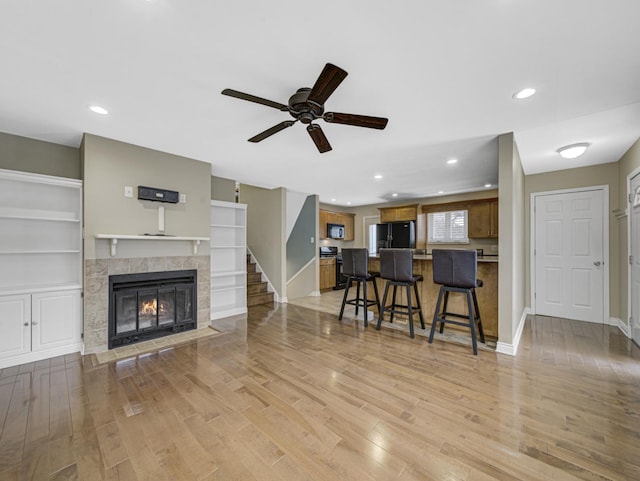 living room with built in features, light hardwood / wood-style flooring, ceiling fan, and a tiled fireplace