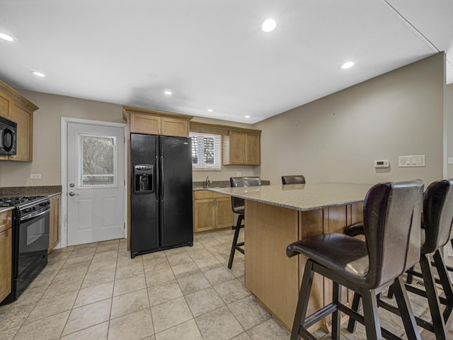 kitchen with light stone countertops, a center island, a breakfast bar area, and black appliances