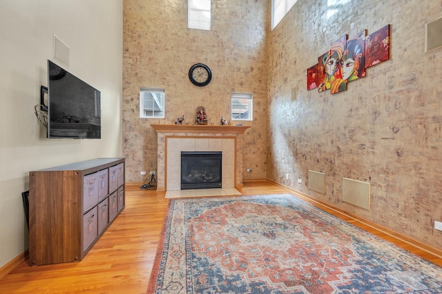 living room with a towering ceiling, a tile fireplace, and light hardwood / wood-style flooring