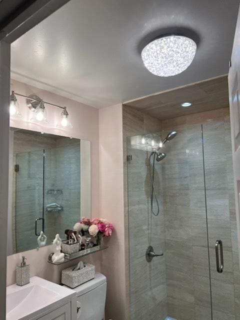 bathroom featuring a shower with door, vanity, and toilet