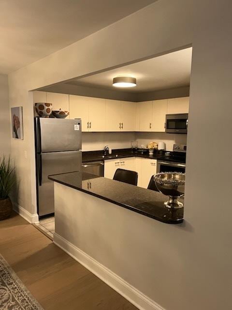 kitchen with kitchen peninsula, appliances with stainless steel finishes, white cabinetry, and hardwood / wood-style floors