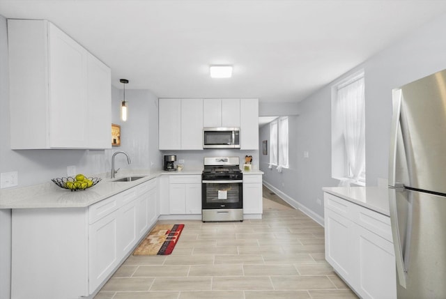 kitchen featuring white cabinetry, sink, decorative light fixtures, and appliances with stainless steel finishes