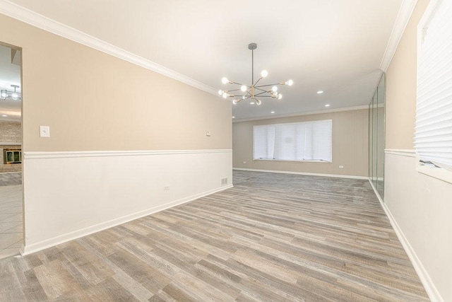 empty room with hardwood / wood-style floors, ornamental molding, a notable chandelier, and a brick fireplace