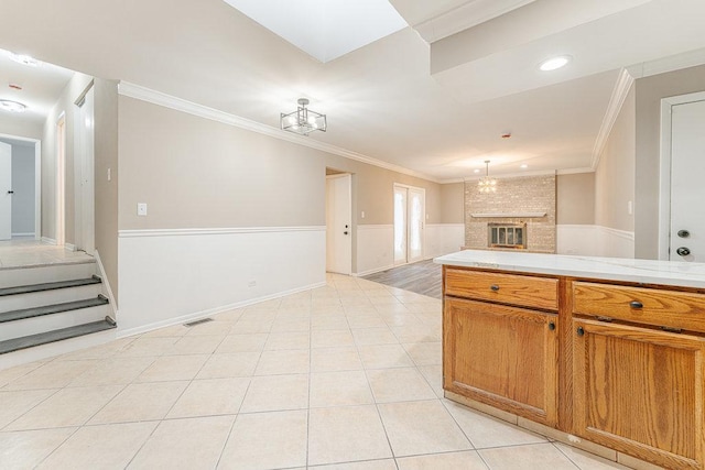 kitchen featuring crown molding, light tile patterned floors, pendant lighting, an inviting chandelier, and a fireplace