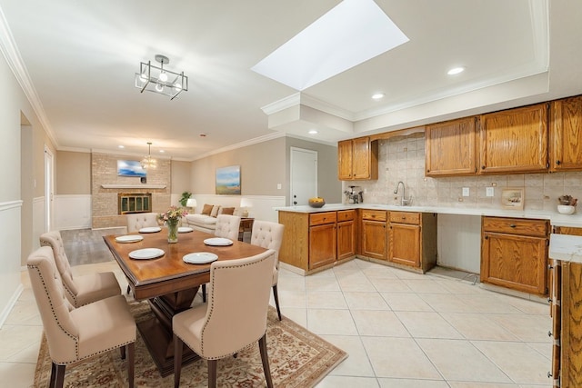 tiled dining space with a fireplace, a skylight, an inviting chandelier, and ornamental molding