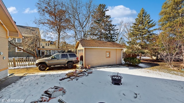 snow covered property with an outbuilding, a fire pit, and a garage