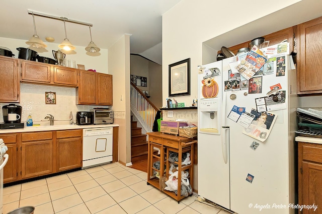 kitchen with decorative light fixtures, vaulted ceiling, light tile patterned floors, white appliances, and decorative backsplash