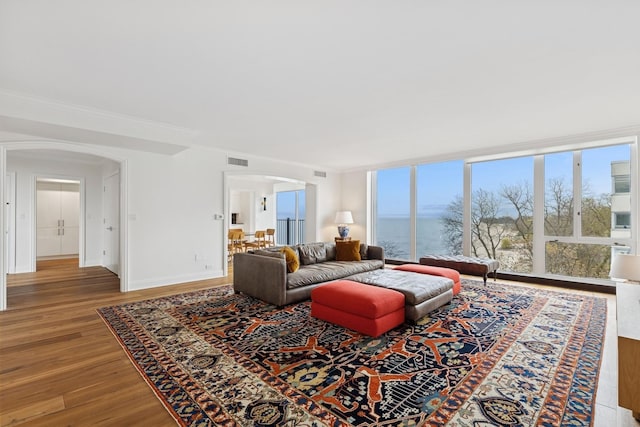 living room with visible vents, ornamental molding, wood finished floors, baseboards, and arched walkways