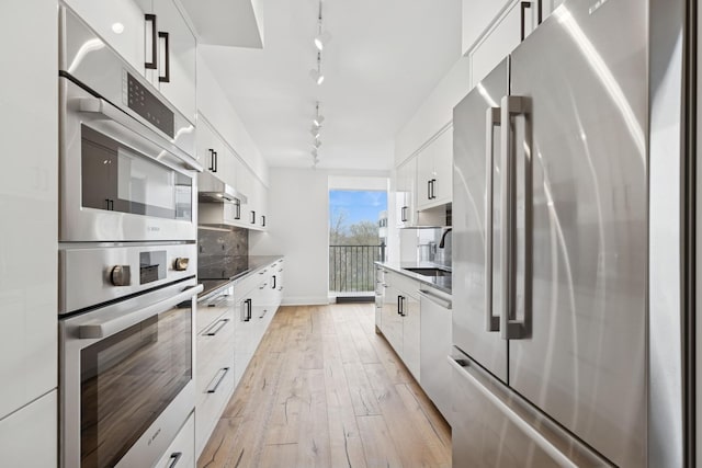 kitchen featuring modern cabinets, a sink, track lighting, stainless steel appliances, and white cabinetry