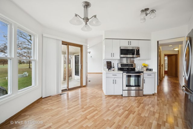 kitchen with white cabinets, backsplash, appliances with stainless steel finishes, and light hardwood / wood-style flooring