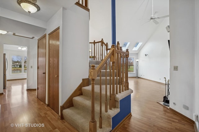 staircase featuring ceiling fan, wood-type flooring, high vaulted ceiling, and a skylight