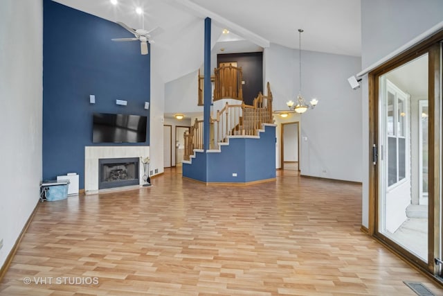 living room featuring light wood-type flooring, ceiling fan with notable chandelier, high vaulted ceiling, and a tiled fireplace