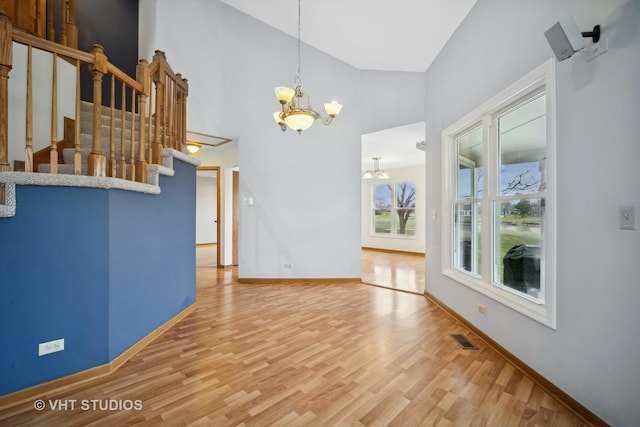 unfurnished living room featuring hardwood / wood-style floors, high vaulted ceiling, and an inviting chandelier