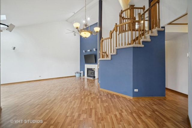 unfurnished living room with hardwood / wood-style floors, a tiled fireplace, high vaulted ceiling, and an inviting chandelier