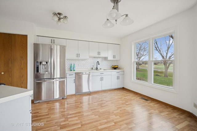 kitchen featuring sink, light wood-type flooring, decorative light fixtures, white cabinetry, and stainless steel appliances