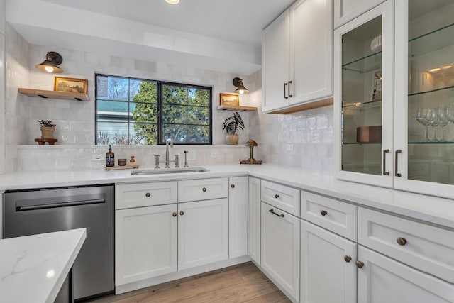 kitchen with white cabinetry, dishwasher, sink, light stone countertops, and decorative backsplash