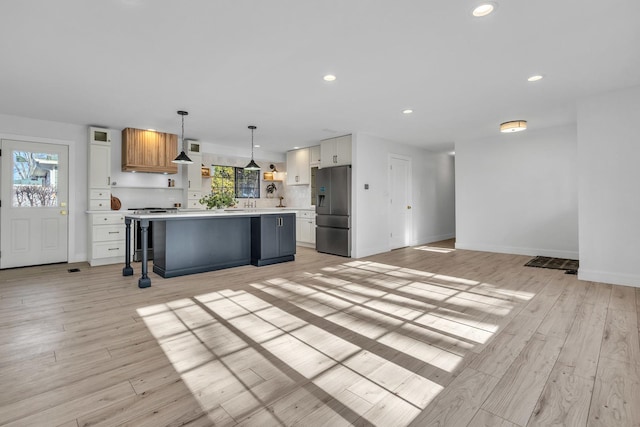 kitchen with white cabinets, stainless steel fridge, a kitchen island, and hanging light fixtures