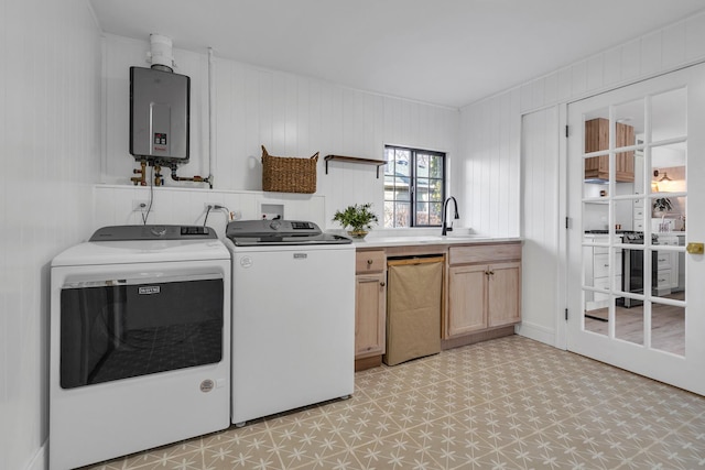 clothes washing area with sink, cabinets, tankless water heater, wooden walls, and washer and clothes dryer